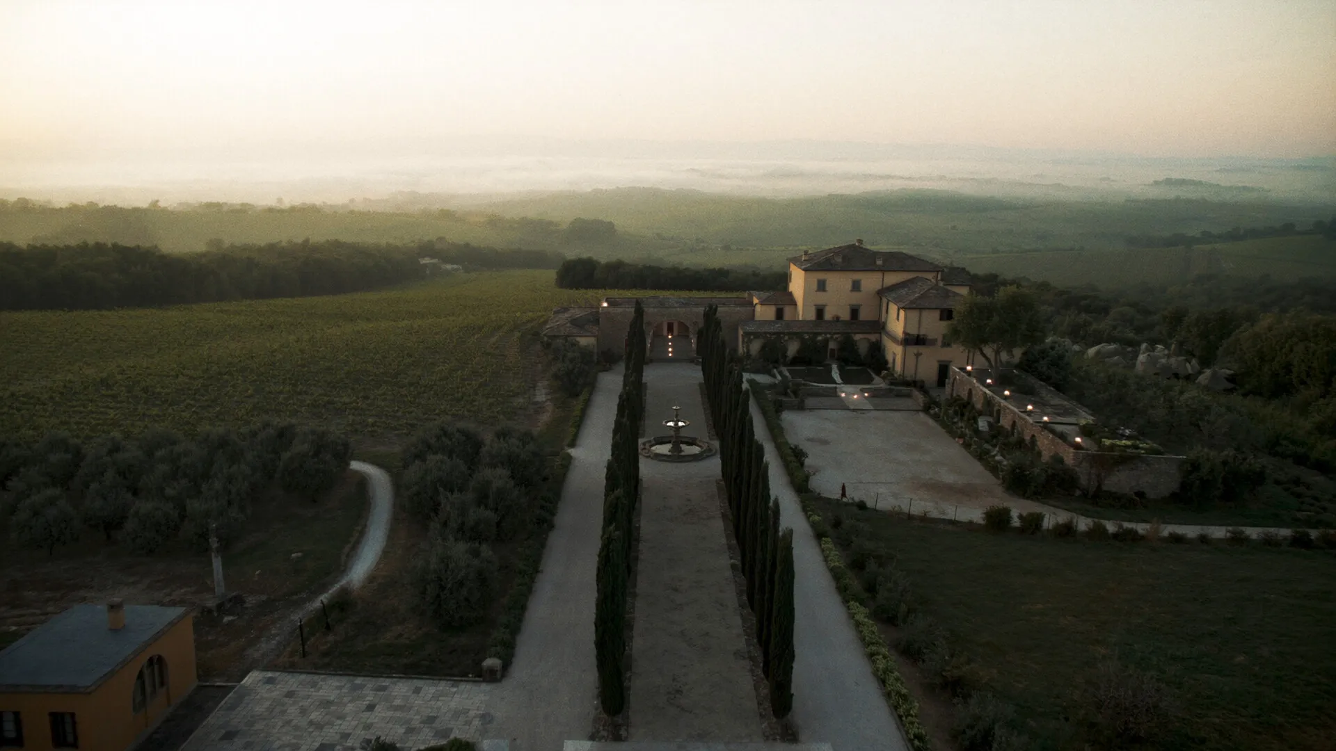 Tenuta vinicola toscana al tramonto, viale di cipressi verso una villa in pietra